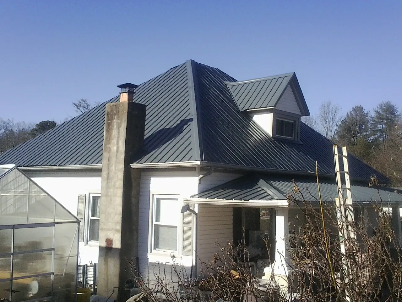 Dark blue standing seam metal roof on a white farmhouse with dormer — Slate & Tile Roof Repair by Roofing Brothers in Los Alamos