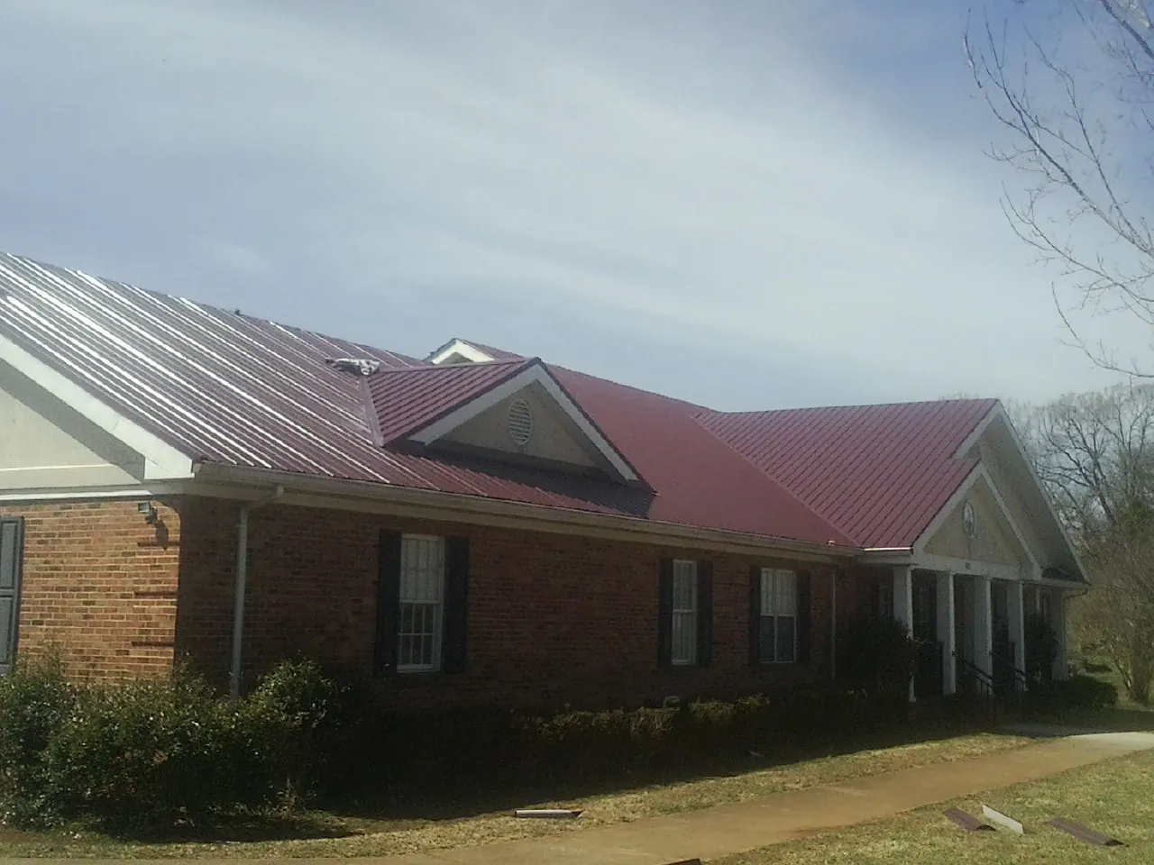 Red metal roof with gabled entries on a long brick building, from a Hail Damage Roof Repair job in Los Alamos
