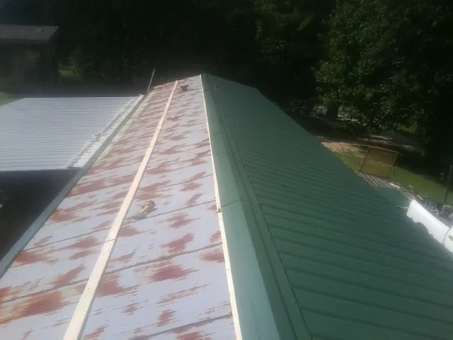 Old rusted panels beside newly installed green metal roofing — Wind Damage Roof Repair by Roofing Brothers in Los Alamos