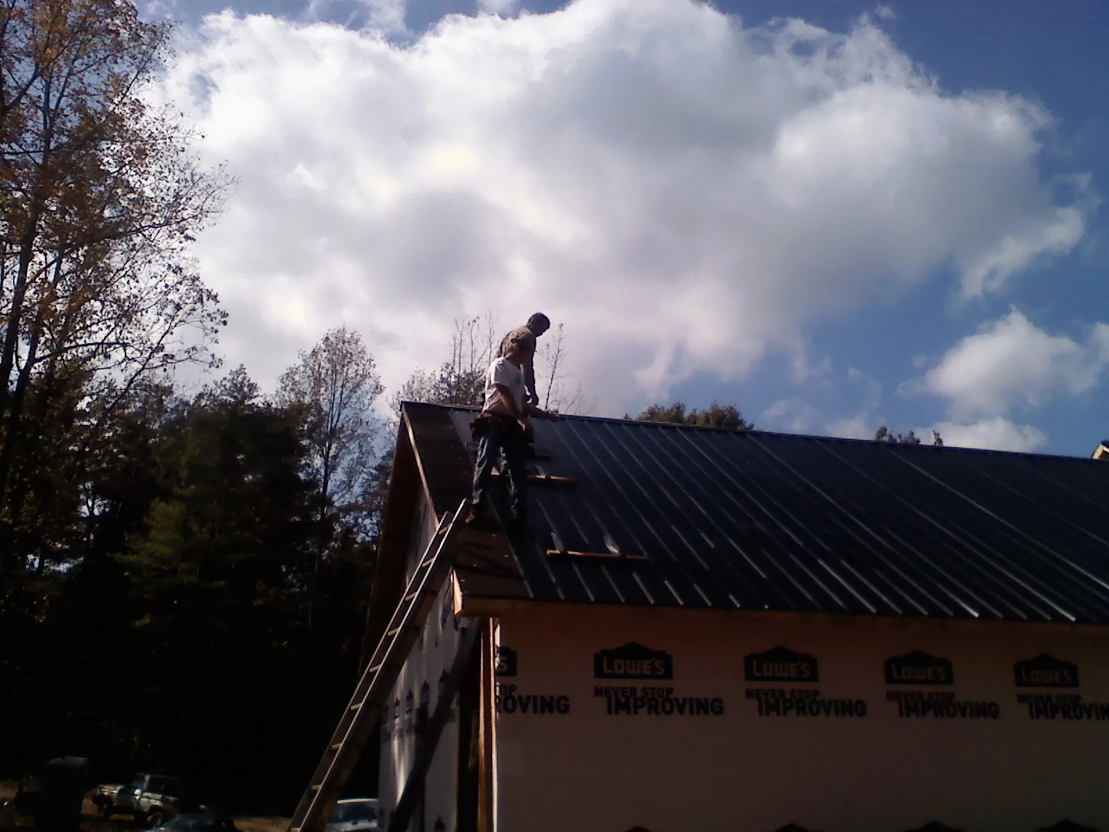 Roofer fastening dark metal panels high against a cloudy sky, from a Roof Inspection job in Los Alamos