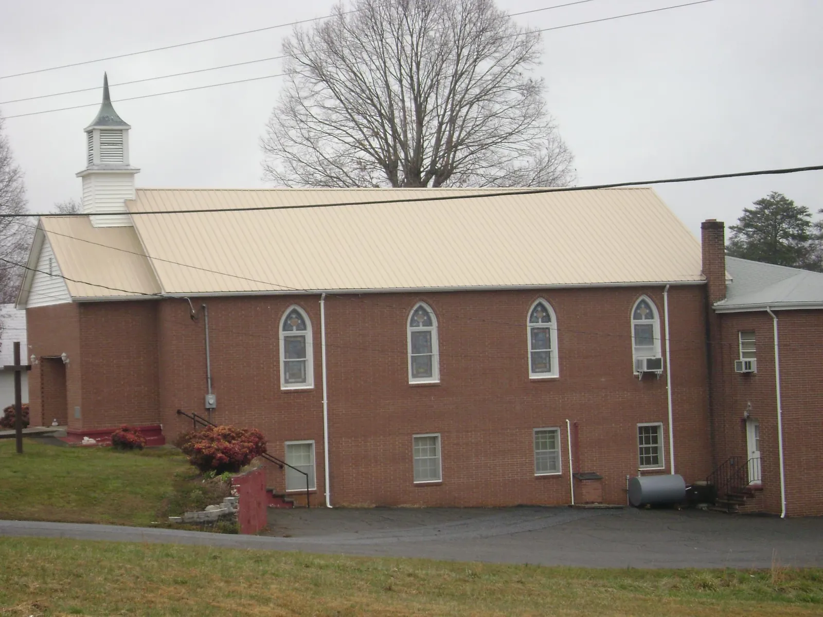 New tan metal roof on a brick church with a white steeple in Los Alamos