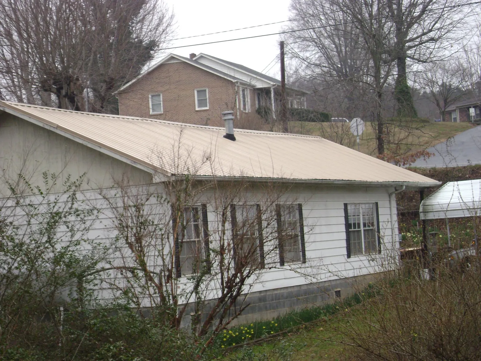 Tan metal roof on a white sided house set into a hillside — Commercial Roofing by Roofing Brothers in Los Alamos