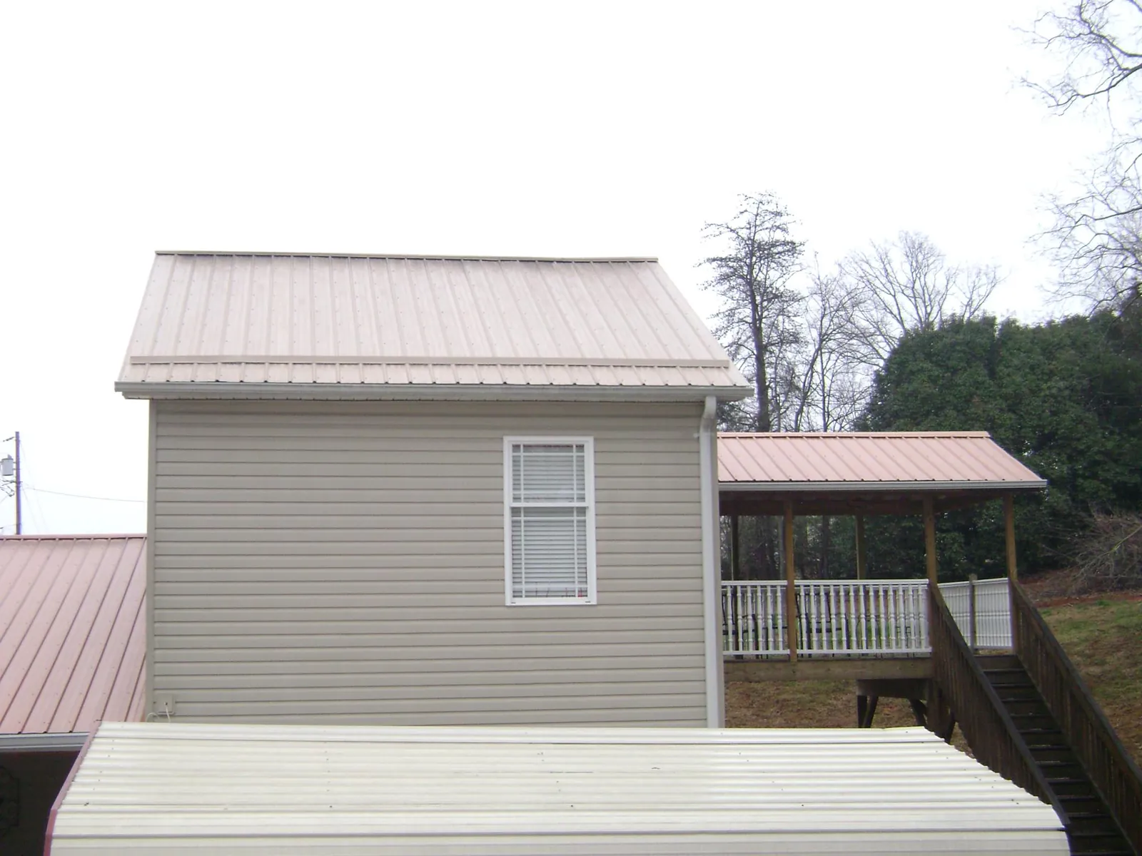 Tan metal roofs on a two story addition and attached porch, from a Roof Replacement job in Los Alamos
